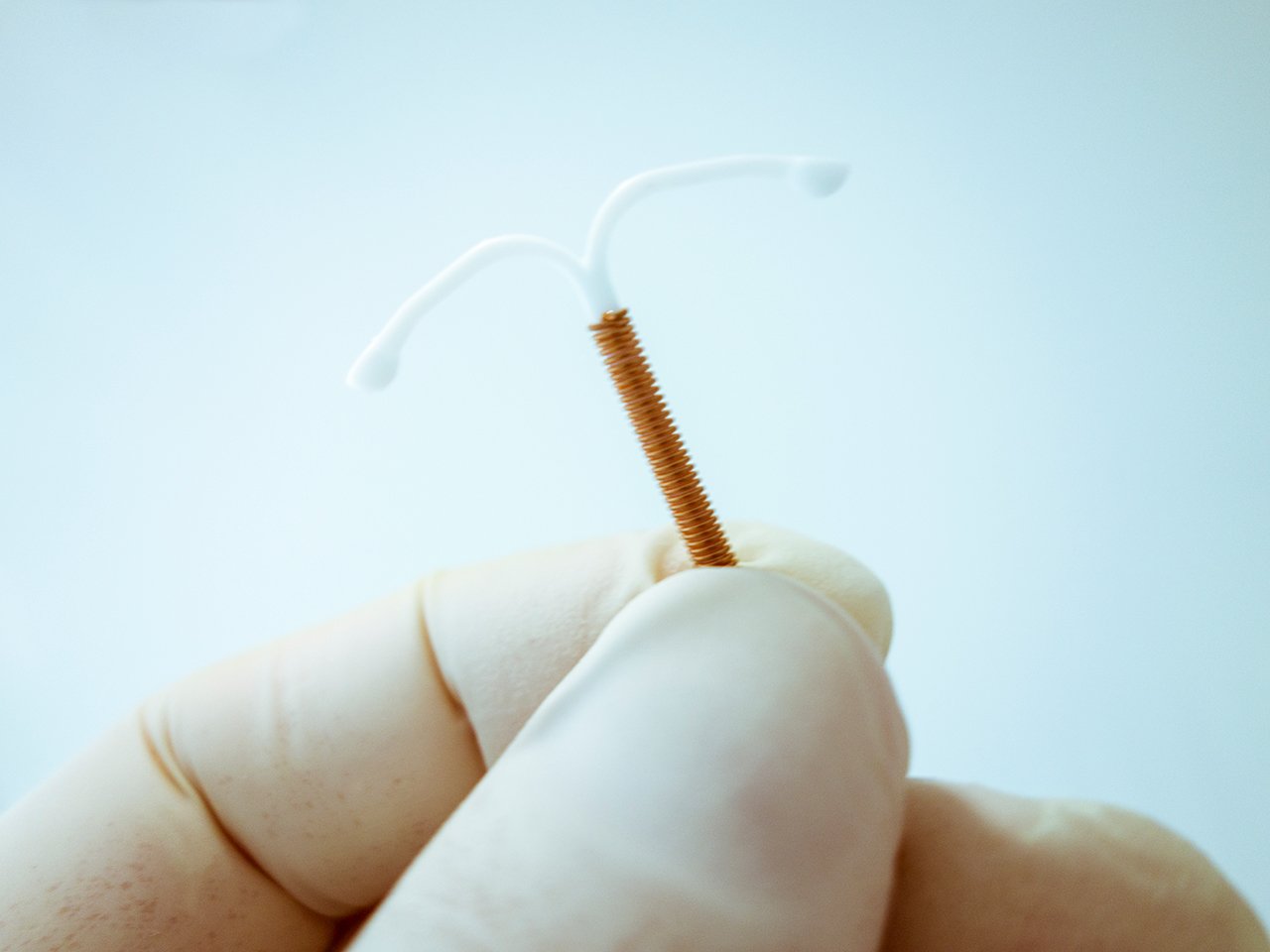 A doctor with a gloved hand holding an IUD.