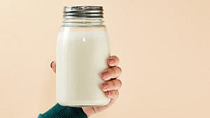 Nut milk recipes: A person's hand holding a mason jar filled with nut milk