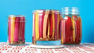 three jars of pickled rainbow chard stems on a tablecloth against a blue background