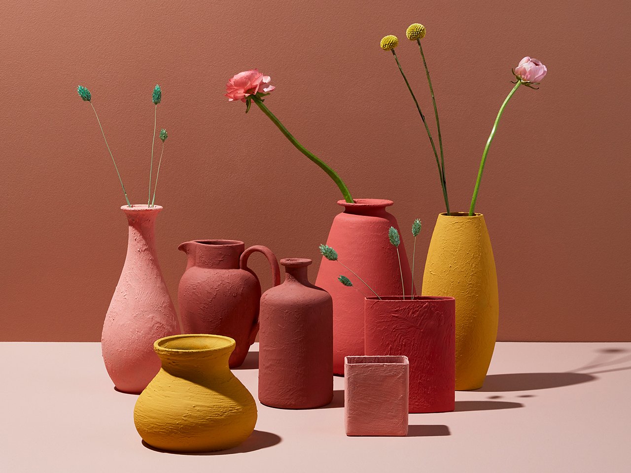 Several painted thrift store vases with flower stalks laid on a surface