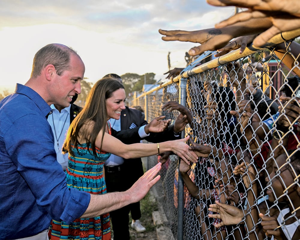 Prince William and Catherine, Duchess of Cambridge, shake hands with schoolchildren in Jamaica through a chain-link fence.
