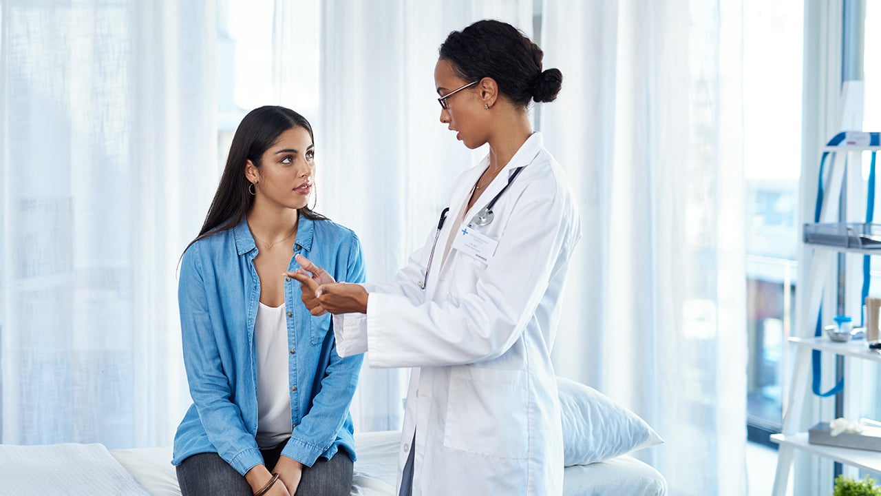 A young woman in a blue blazer having a consultation with her female doctor