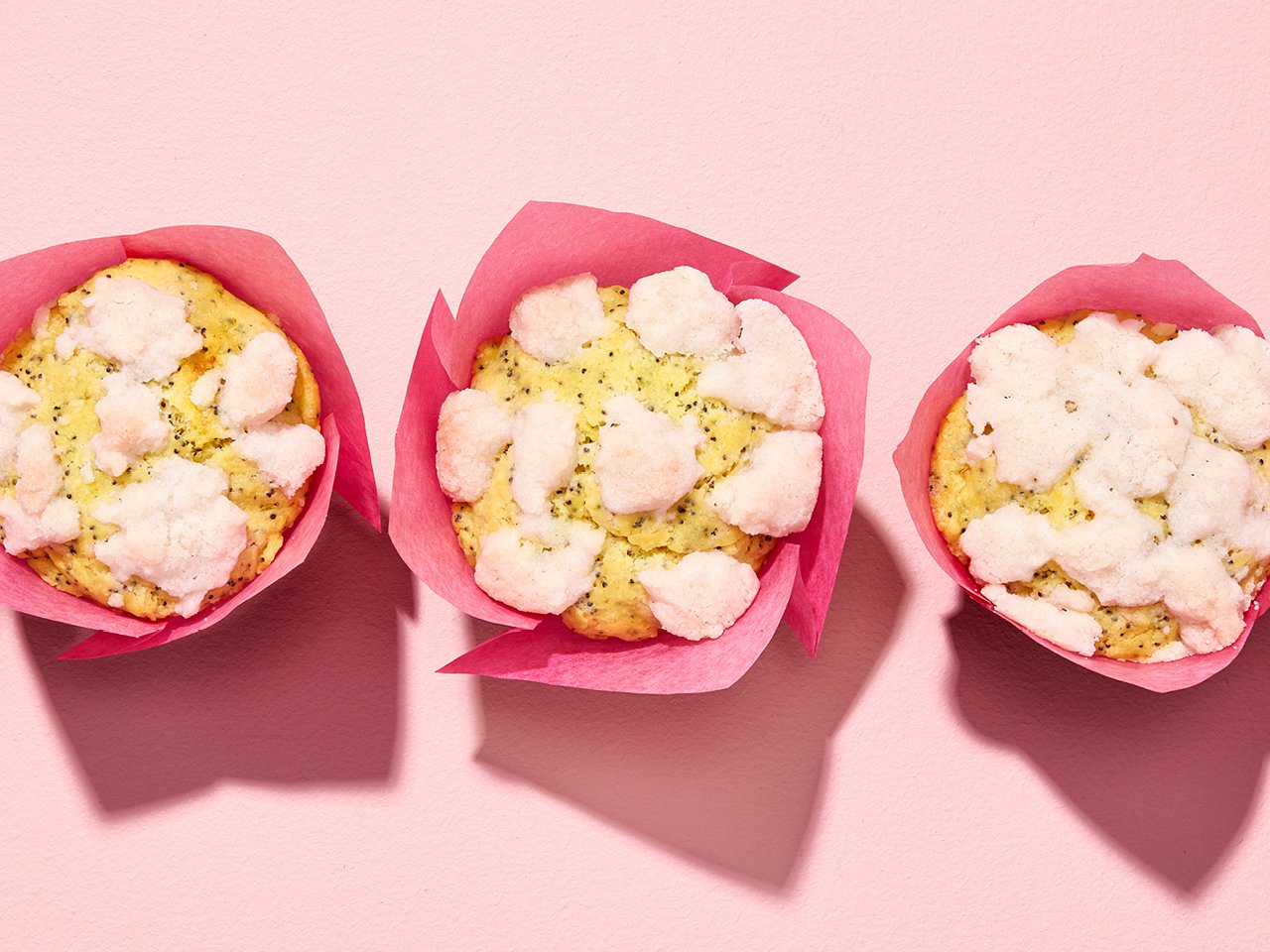 Five lemon poppy seed streusel muffins in pink wrappers on pink backdrop.