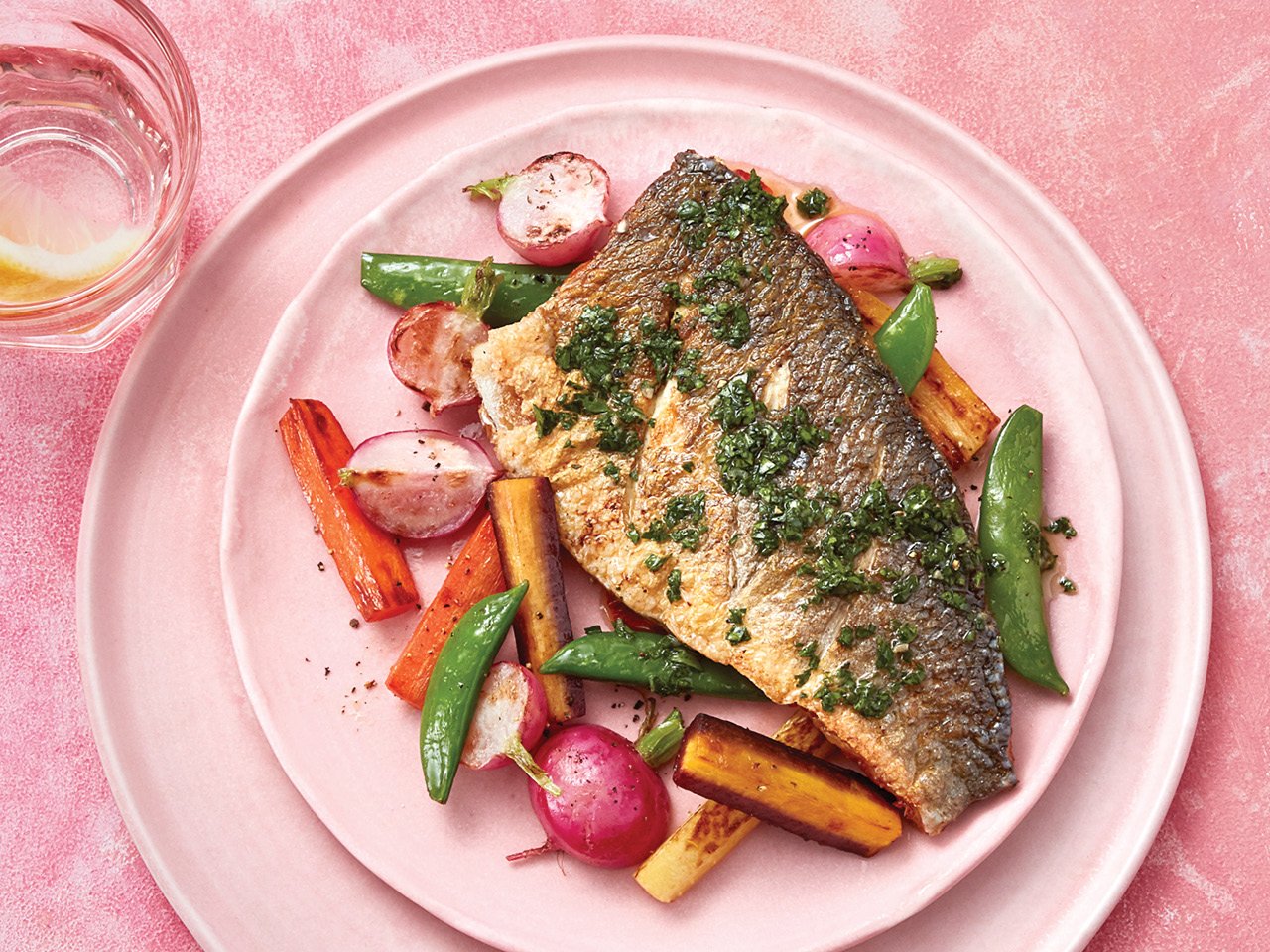 Pan fried Mediterranean sea bass and vegetables on pink plate on pink table.