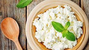 ricotta in beige wooden bowl with wooden spoon and mint on top.