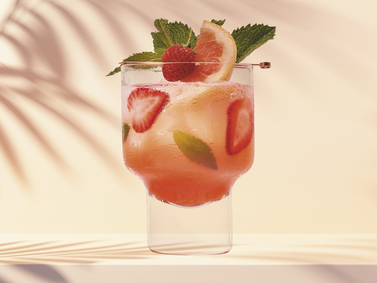 Strawberry grapefruit cocktail in a glass, wth mint leaves. In front of a beige background.