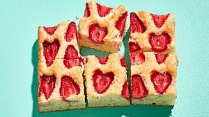 A section of pale yellow snacking cake with inlaid strawberries sliced into six pieces on a turquoise table