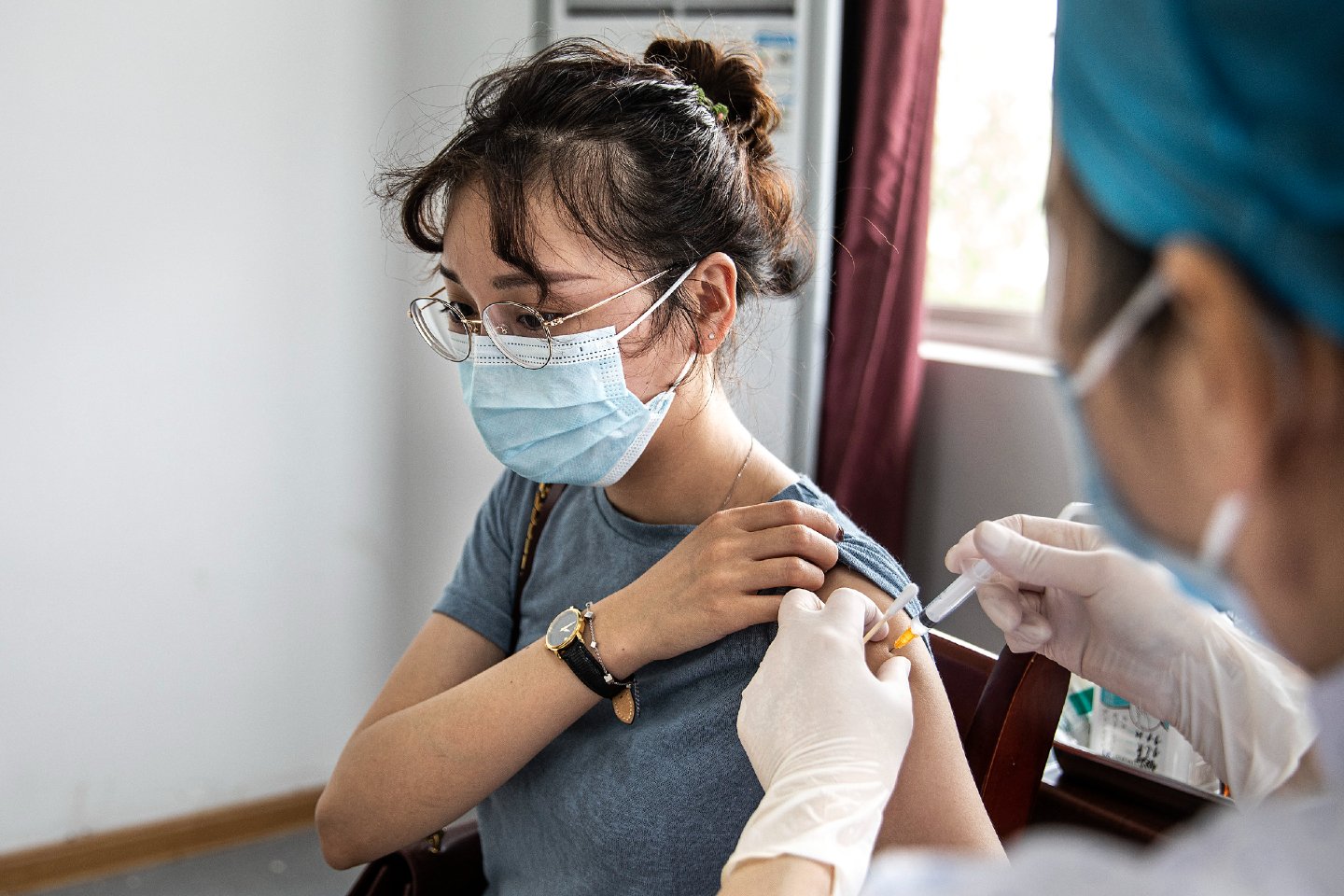 A woman pulls her shirt sleeve up while she's getting a COVID-19 vaccine shot from a healthcare worker 