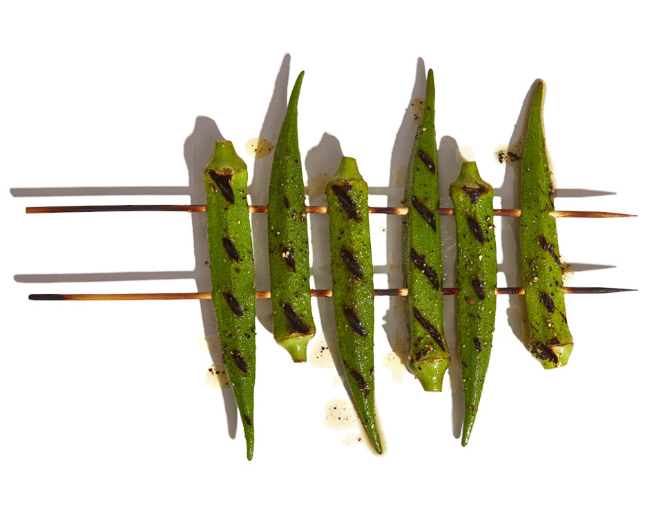 A close up of grilled okra on two wood skewers on a white background