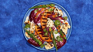 A blue plate on a blue tablecloth filled with grilled okra and cantaloupe salad