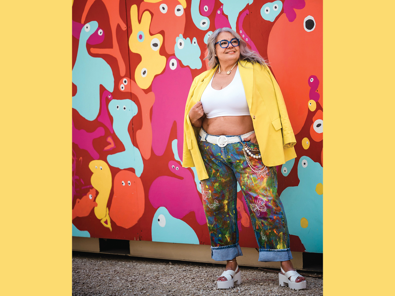 Influencer Manny Martins-Karma wearing painted jeans and a bright yellow blazer against a colourful mural.