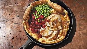 A pan with a Dutch baby filled with chicken, peas and cranberries wooden work surface.