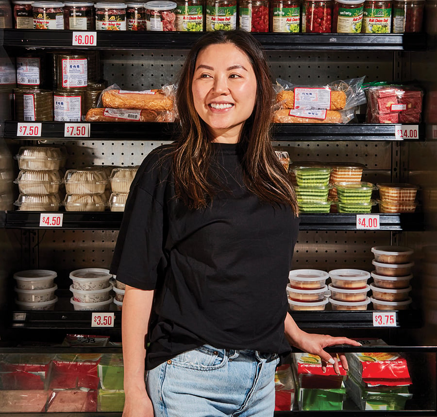 Chef Tara Le in front of an open cold fridge with shelves of packaged foods