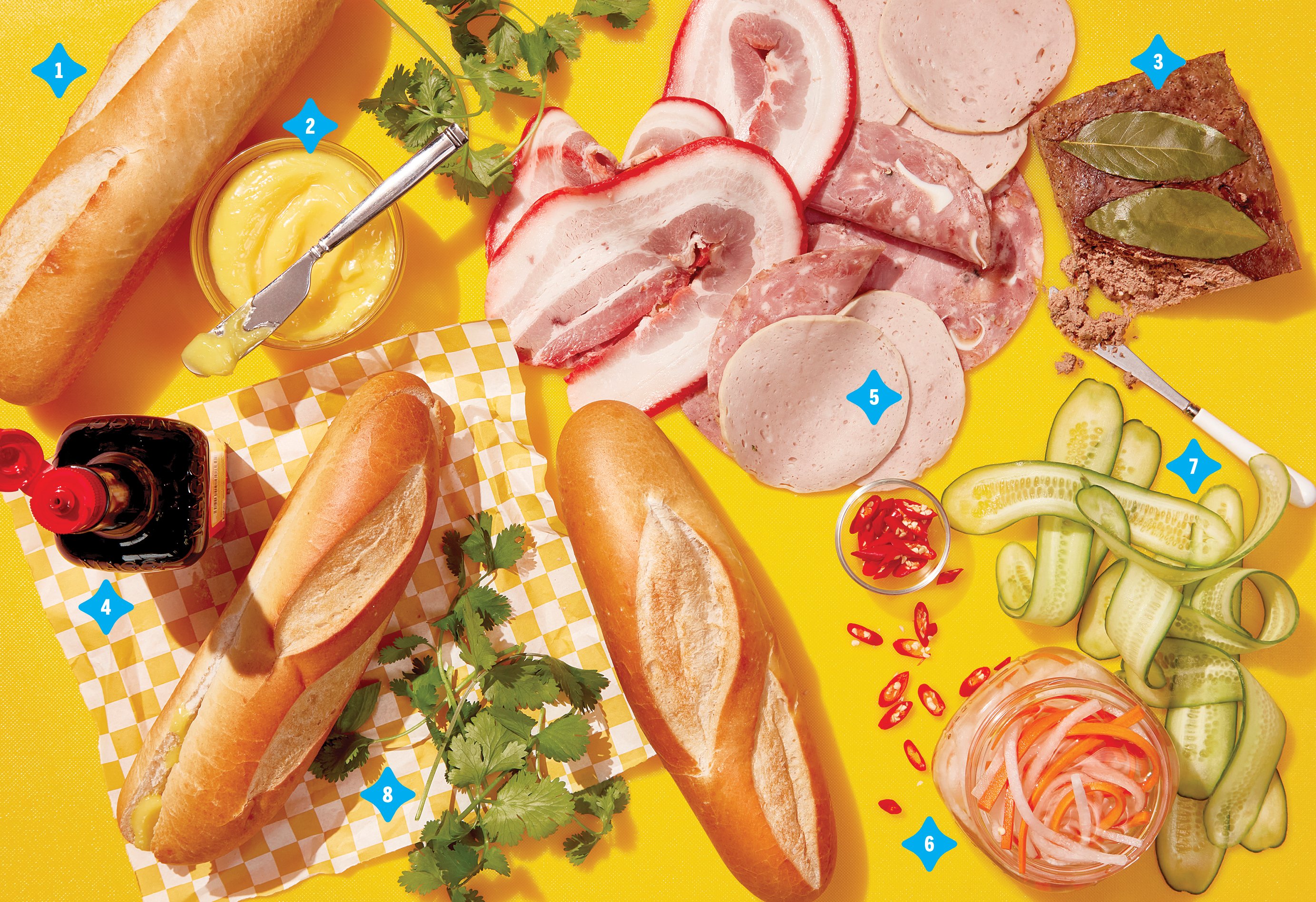An array of banh mi essentials on a yellow background, including Maggi sauce, baguettes, bo, pate, and cucumbers
