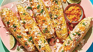 5 pieces of corn on the cob with various white sauces, orange flakes and green sprigs haphazardly arranged on top.