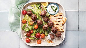 A plate with kofta kebabs and a plate of salad and bread on it.