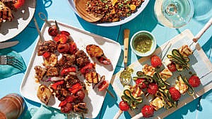 two kebab dishes and a white berry salad on a blue table