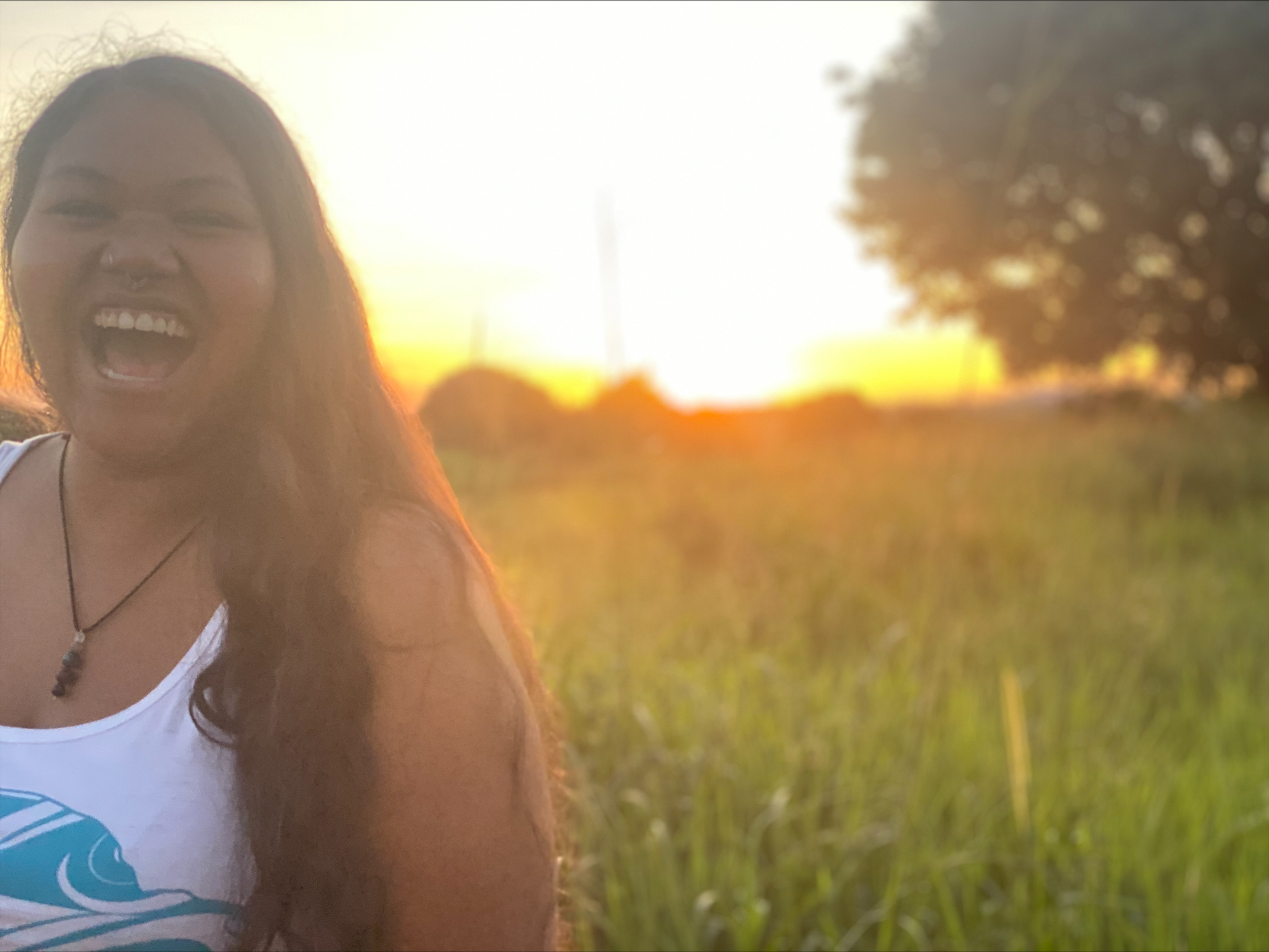 A photograph of a woman laughing in a field with the sun setting in the background