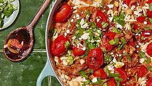 A pan of toasted orzo, chickpea and tomato stoup beside a wooden spoon
