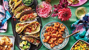 An array of homemade taco bar fillings laid out on a table with tacos and serving dishes and toppings for a feature on how to build a DIY taco bar