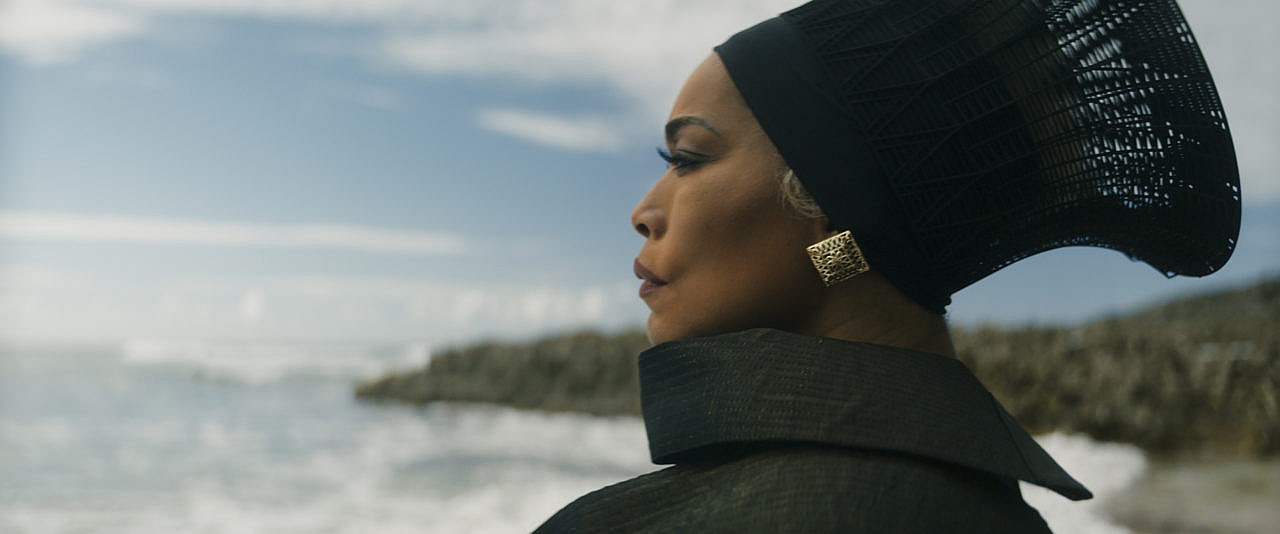 A side profile of a woman looking out to the sea; she is wearing a black head covering and gold earrings.