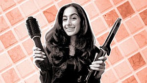 A woman with a blowout holding a blow dryer hair brush and hair curler.