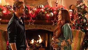 Falling For Christmas. (L to R) Chord Overstreet as Jake Russell, Lindsay Lohan as Sierra Belmont in Falling For Christmas, standing in front of a roaring fire with Christmas decorations in the background