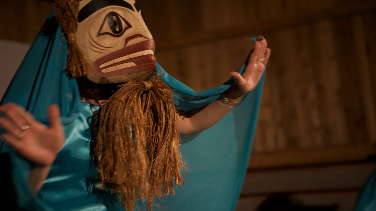 A woman wears a costume depicting a Haida supernatural character on stage.