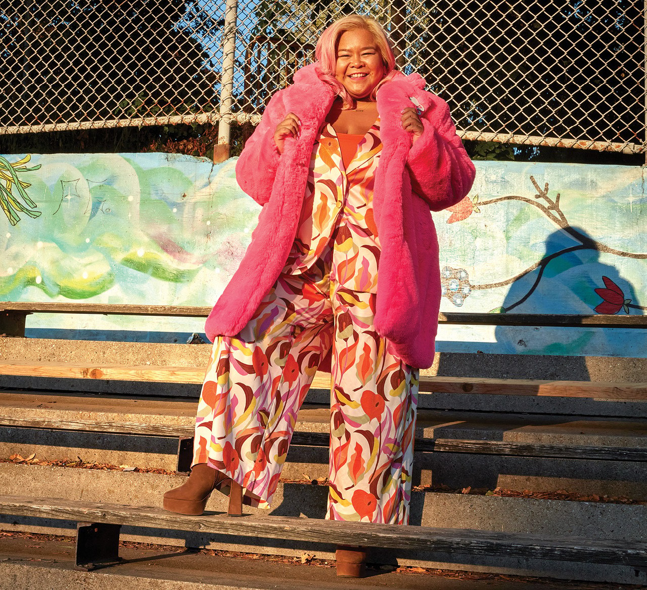 TV host Ann Ponell wore a wide-leg orange leaf-print suit, a pink faux-fur jacket, and a silk-orange croissant bag for a photo in the park.