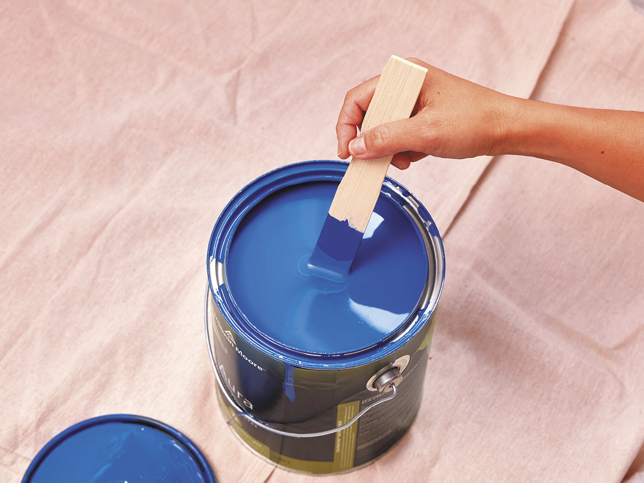 A bucket of blue paint with a stick stirring.