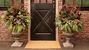 Two DIY holiday urn arrangements pictured flanking a black door on a porch.
