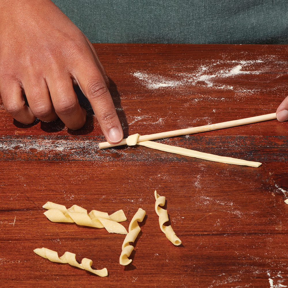 Busiate pasta dough being rolled around a wooden skewer