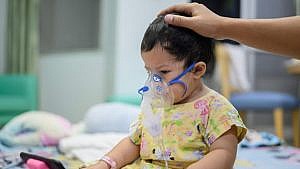 A child in a patterned hospital gown wearing an oxygen mask