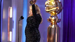 A side profile of a woman in a long-sleeved black glittery dress holding a Golden Globe Award in the air