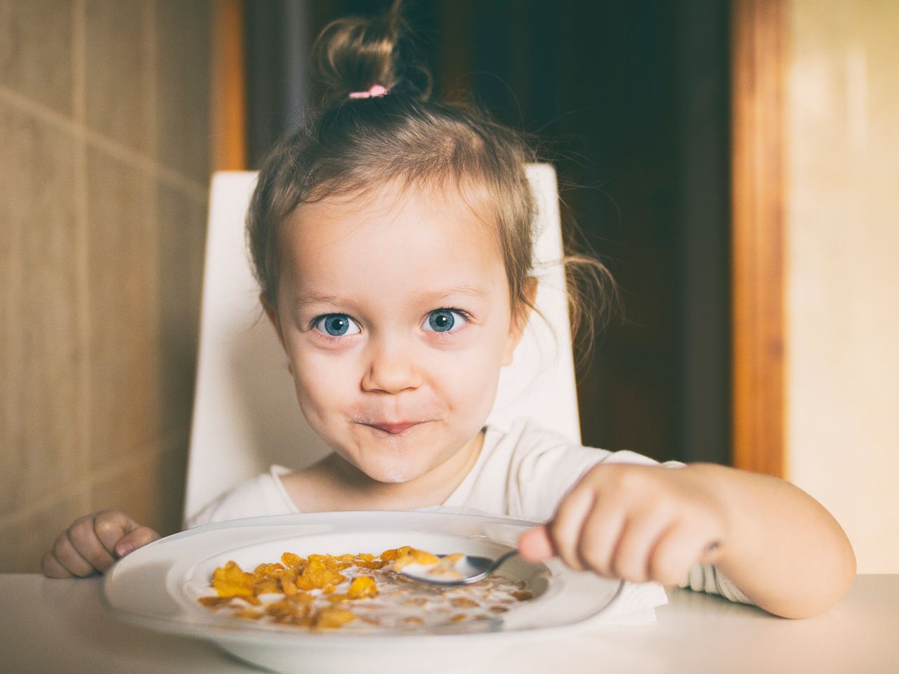 A little kid smiles while eating a bowl of cereal
