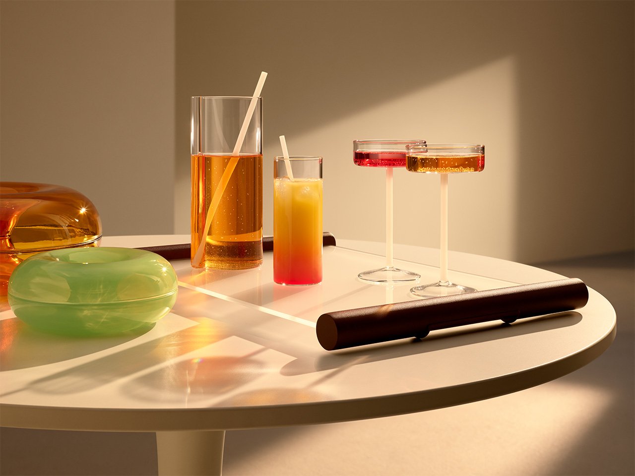 Platos de donas naranjas y verdes y vasos y tazas transparentes de la colección IKEA Varmblixt sobre la mesa