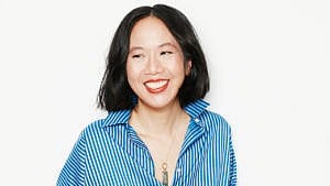 Author Jen Sookfong Lee on a white background, smiling and wearing a blue vertical striped blouse