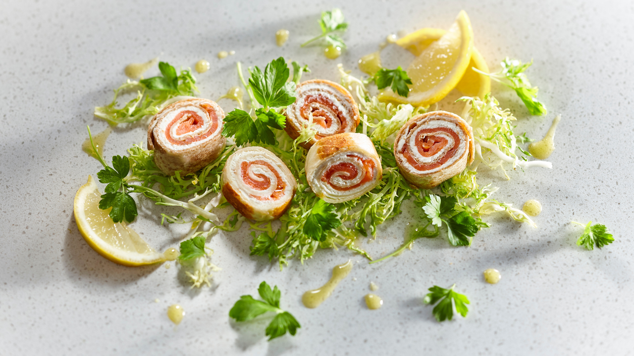 Cut smoked salmon rolls sit on a bed of parsley directly on a countertop