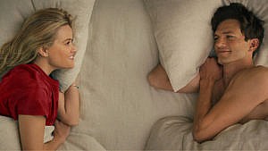 A photo of a man and woman lying on their sides facing each other in bed.